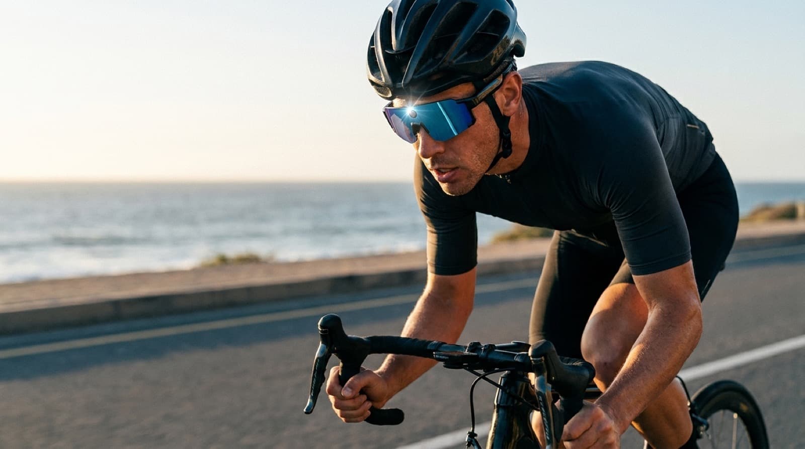 A cyclist wearing OXIVUE M14 sports AI glasses on a coastal road